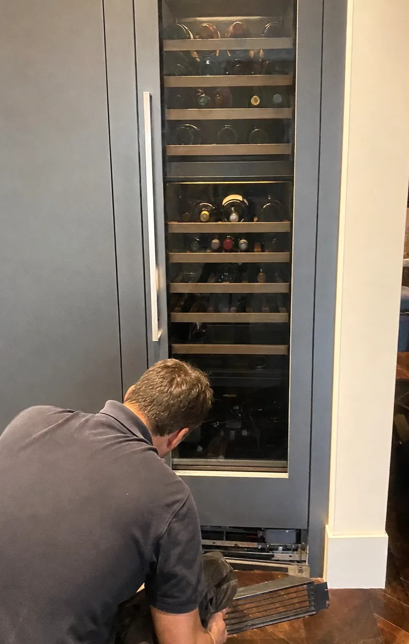 Centre crop of the integrated column in its cabinetry run, glass door closed and the interior light throwing shadows across the bottles.